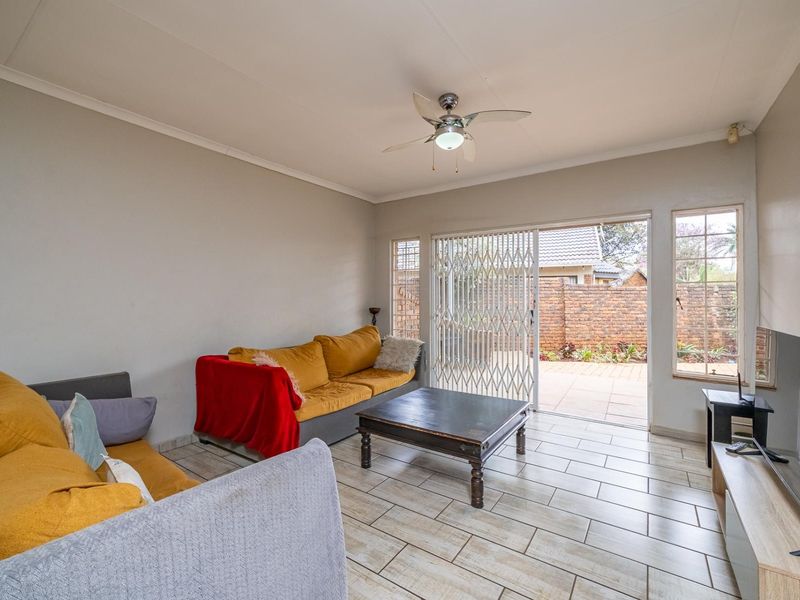 A bright living room featuring tiled flooring, a ceiling fan, and a sliding glass door providing access to the rear patio area.