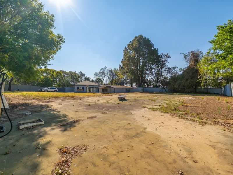 A spacious rear yard featuring a large concrete slab, perimeter walling, and mature trees, offering significant potential for landscaping or development.