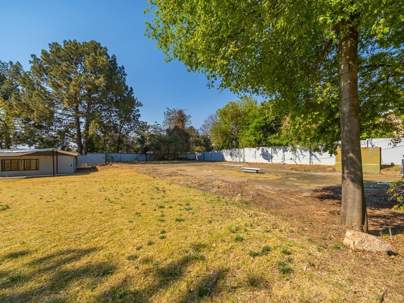 A spacious residential plot featuring a large lawn, mature trees, a concrete slab area, and perimeter walling.