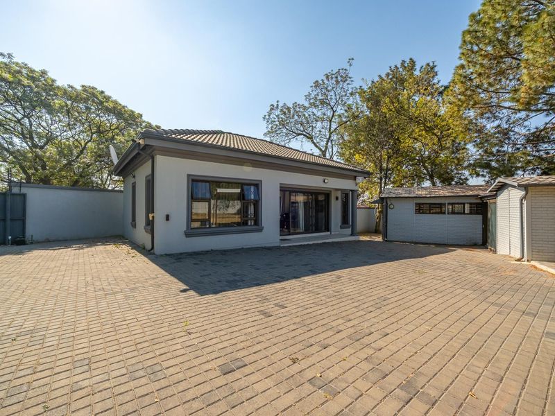 A well-maintained residential property featuring a spacious paved driveway, modern exterior finishes, and established surrounding trees.