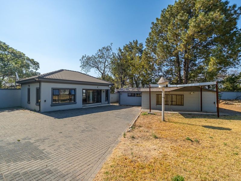 Front view of the property featuring a paved driveway, main dwelling with tiled roof, and a secondary structure with a covered patio area.