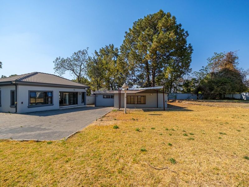 Rear view of the property featuring a paved driveway, covered patio area, and a spacious garden with mature trees.