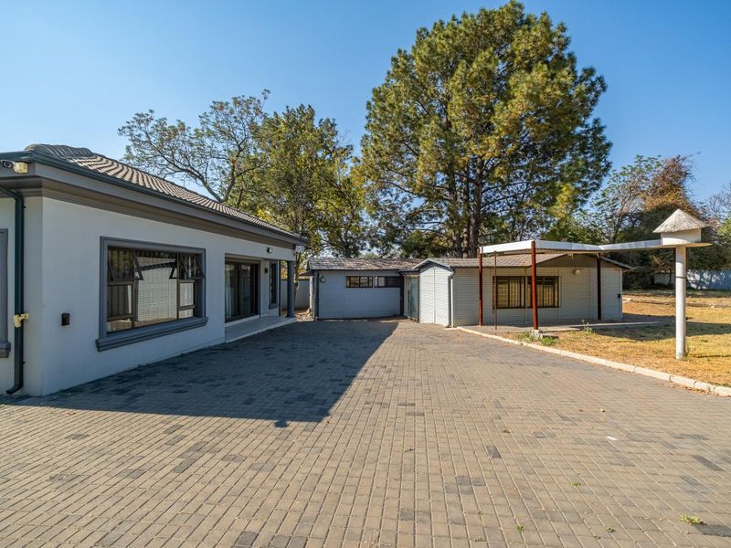 A well-maintained residential property exterior featuring a spacious paved driveway, clean facade, and a covered patio area set within a landscaped garden.