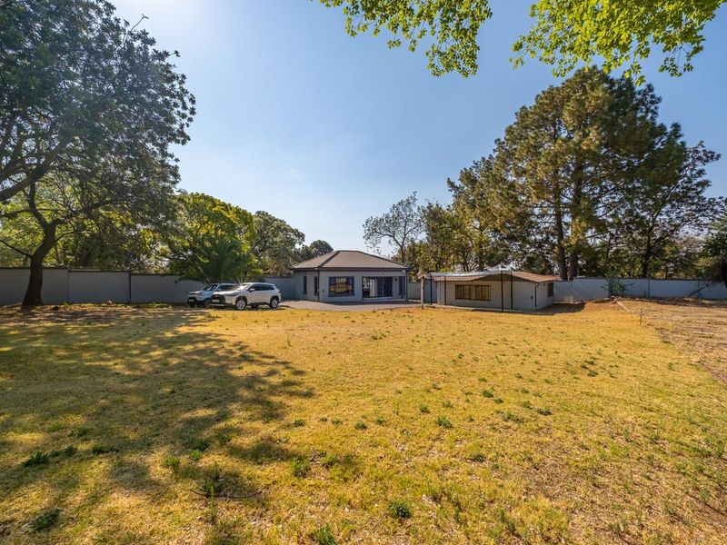 A spacious residential property featuring a main dwelling and outbuilding set within a large, tree-lined garden with perimeter walling.