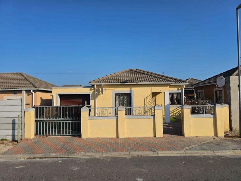 Front elevation of a single-story house featuring a tiled roof, paved driveway, perimeter wall with metal gate, and an integrated garage.