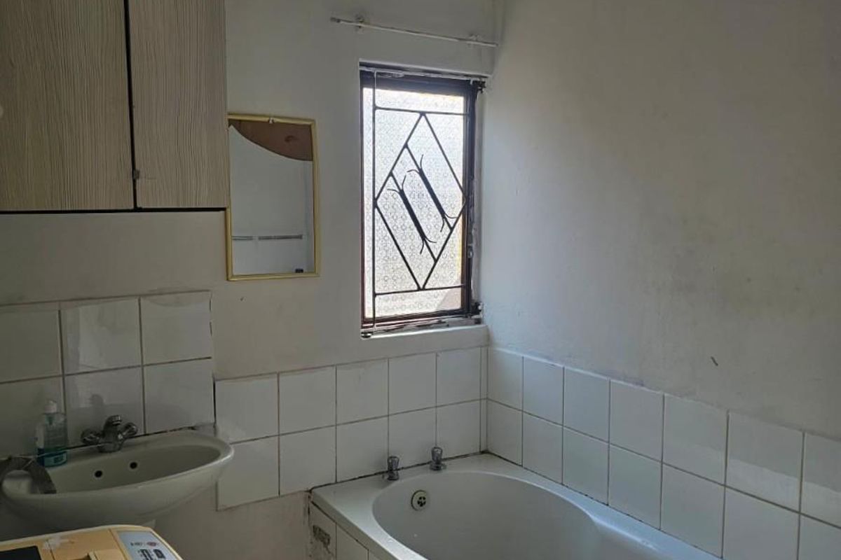 A functional bathroom featuring a bathtub, wall-mounted vanity cabinet, and tiled splashbacks, currently showing signs of wear and requiring cosmetic updates.