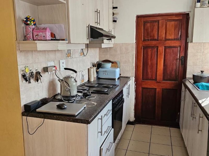 A functional galley-style kitchen featuring built-in cabinetry, an electric hob, oven, and tiled finishes, offering a practical layout for daily meal preparation.