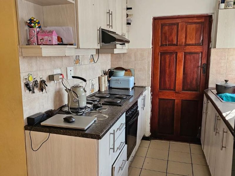 A functional galley-style kitchen featuring light-toned cabinetry, dark countertops, an integrated hob and oven, and tiled flooring with a classic timber door.