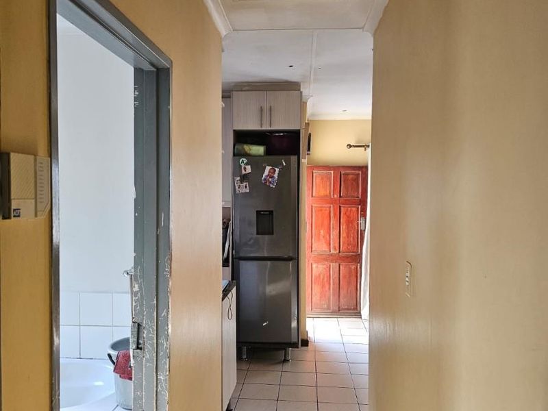 A narrow hallway with tiled flooring, connecting to a bathroom and leading towards a rear timber door.