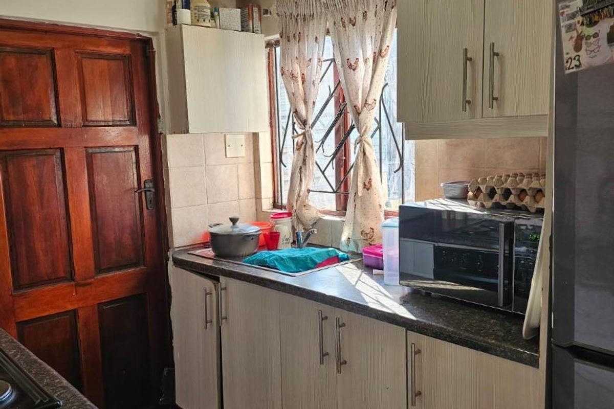 A functional kitchen featuring light-toned cabinetry, stone-look laminate countertops, tiled flooring, and a window with security bars.