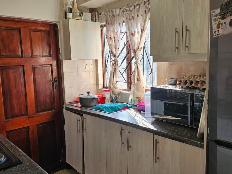 A functional kitchen featuring light-toned cabinetry, stone-look laminate countertops, tiled flooring, and a window with security bars.