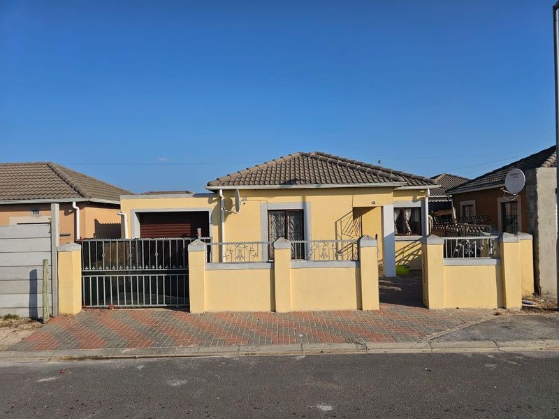 Front elevation of a single-story house featuring a tiled roof, paved driveway, and a gated boundary wall with security features.