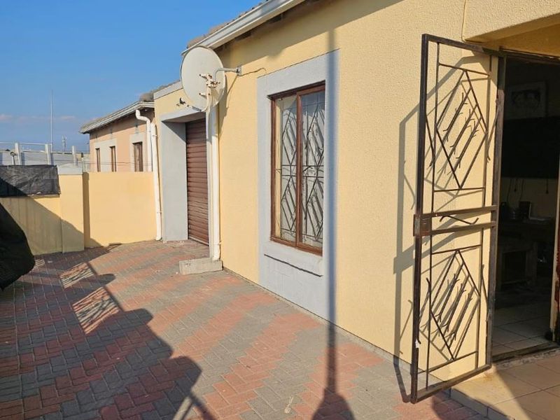Front exterior view of the house featuring paved driveway, security gate, and security bars on the windows.