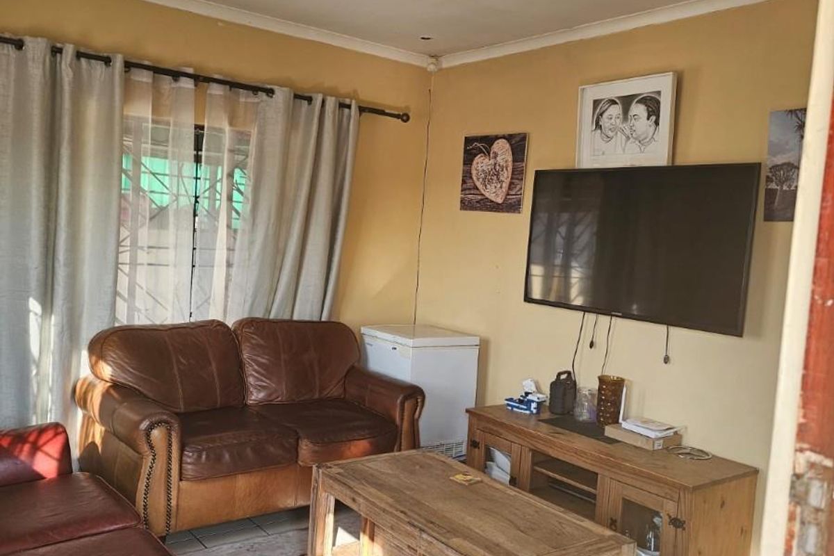 A living room featuring tiled flooring and curtain rails, showing signs of wear including ceiling paint deterioration and wall cracks.