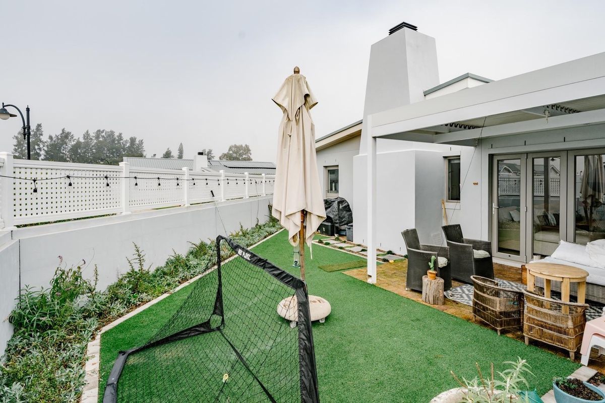 Rear garden area featuring a covered patio, artificial lawn, and a prominent outdoor fireplace structure.