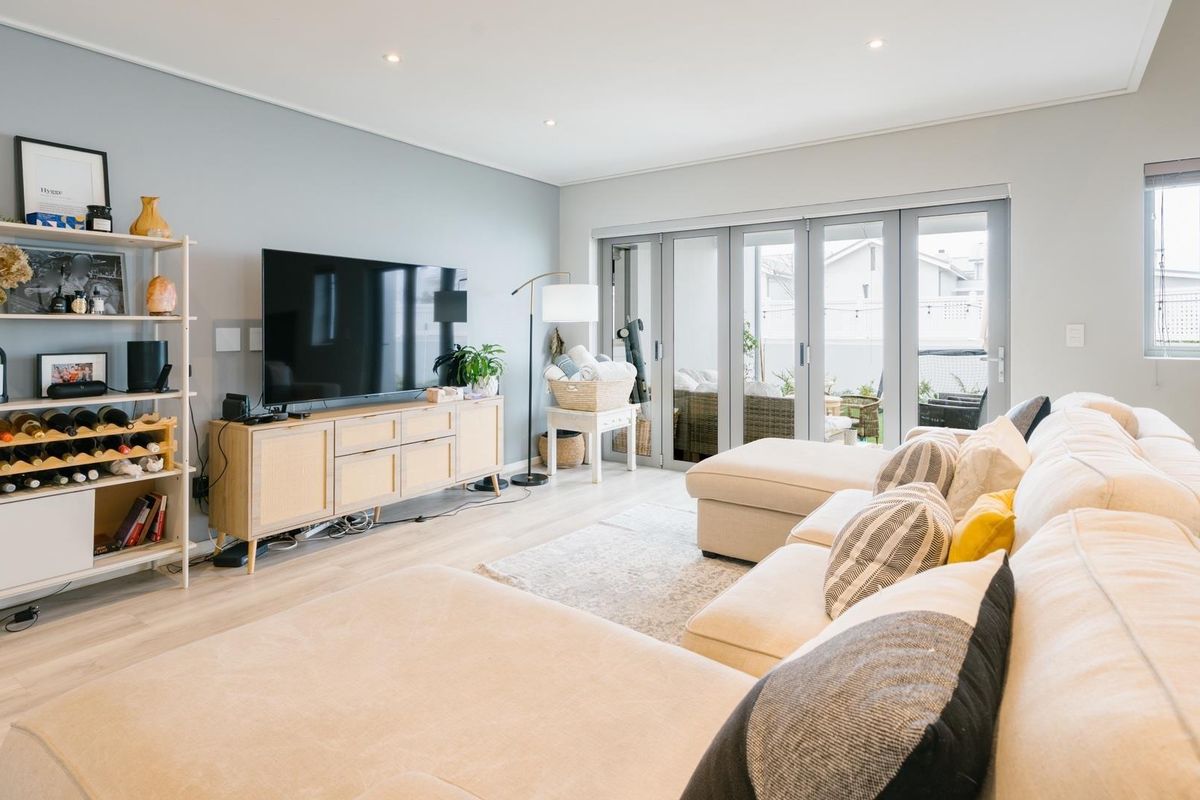 A bright and modern living room featuring light laminate flooring, recessed downlighting, and large aluminium stacker doors providing seamless access to the outdoor patio area.