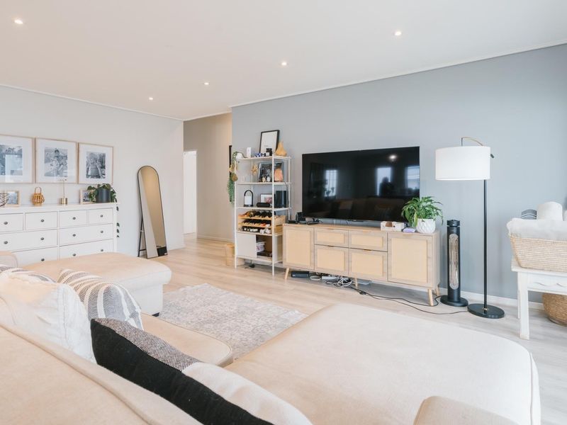 A bright and modern living room featuring light-toned laminate flooring, recessed downlighting, and a large sliding glass door providing access to the outdoors.