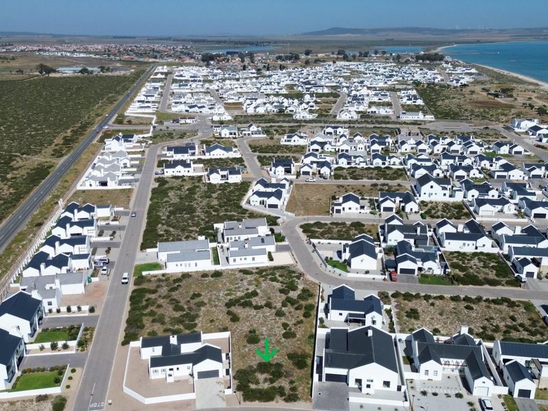 Aerial view of a vacant residential plot situated within a developed coastal estate, featuring established road infrastructure and surrounding residential properties.