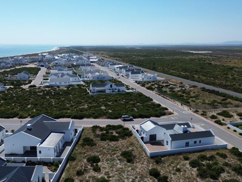 An aerial view of a coastal residential estate featuring modern white homes, paved streets, and surrounding natural vegetation near the ocean.