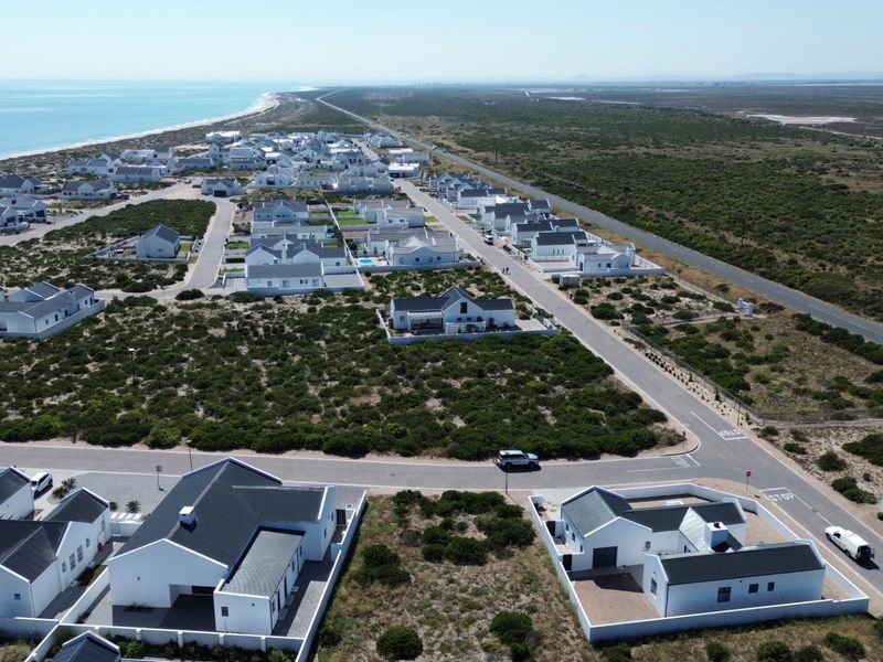 Aerial view of a coastal residential estate featuring modern white homes, paved streets, and proximity to the ocean.
