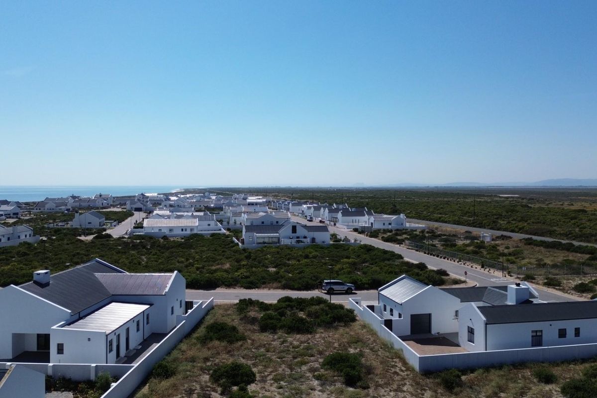 An aerial view of a coastal residential estate featuring modern white homes, paved streets, and surrounding natural vegetation.