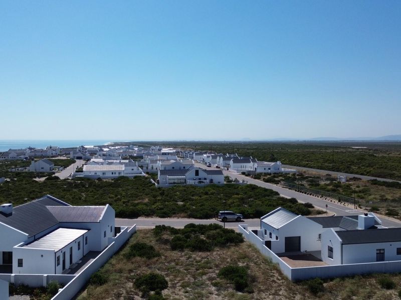 An aerial view of a coastal residential estate featuring modern white homes, paved streets, and surrounding natural vegetation.
