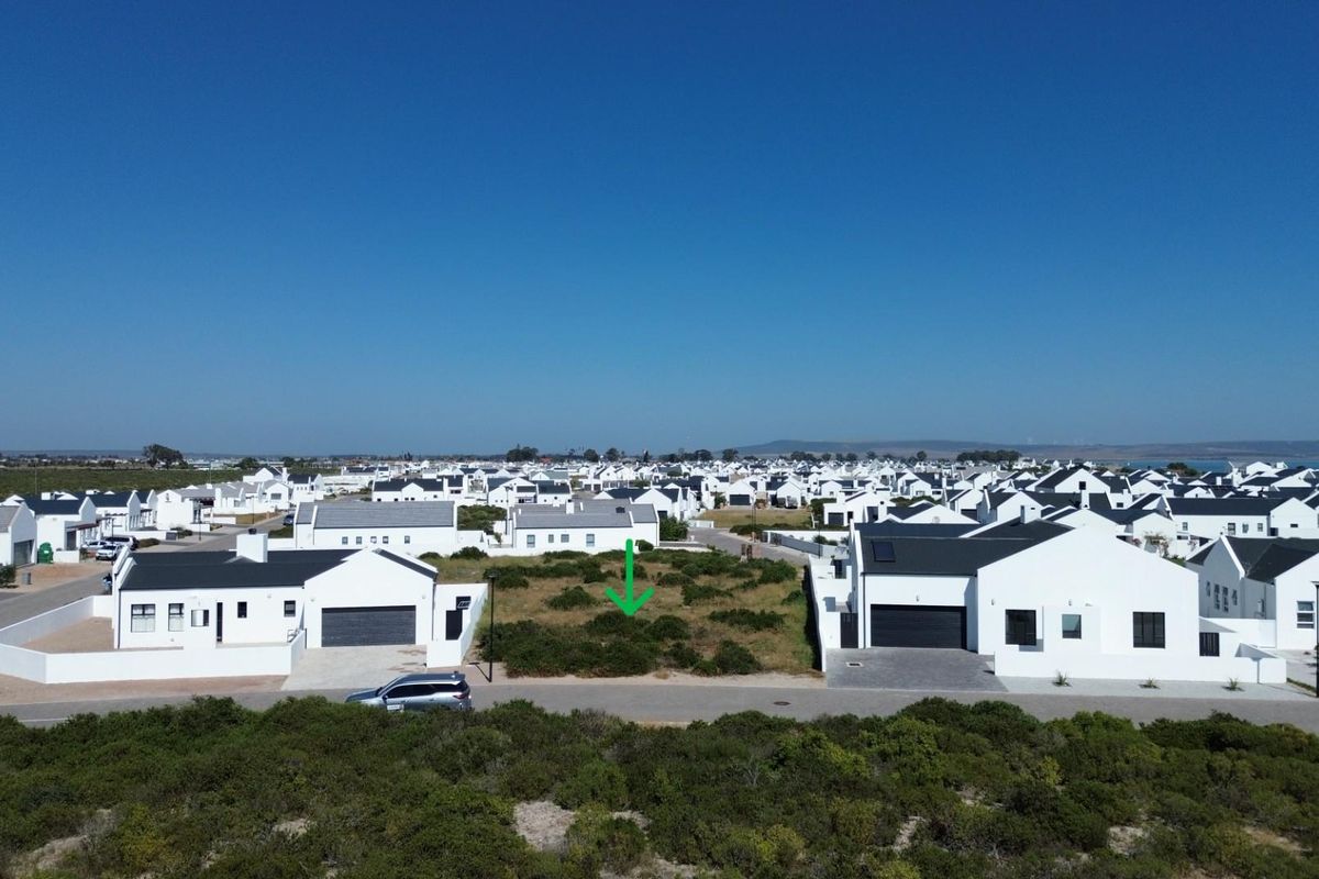 Aerial view of a vacant residential plot situated within a developed coastal estate, featuring street access and established neighboring properties.