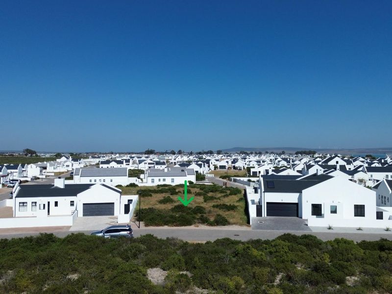 Aerial view of a vacant residential plot situated within a developed coastal estate, featuring street access and established neighboring properties.