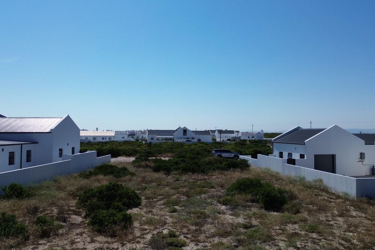 Aerial view of a residential plot featuring surrounding white-walled homes with metal roofs and natural coastal vegetation.