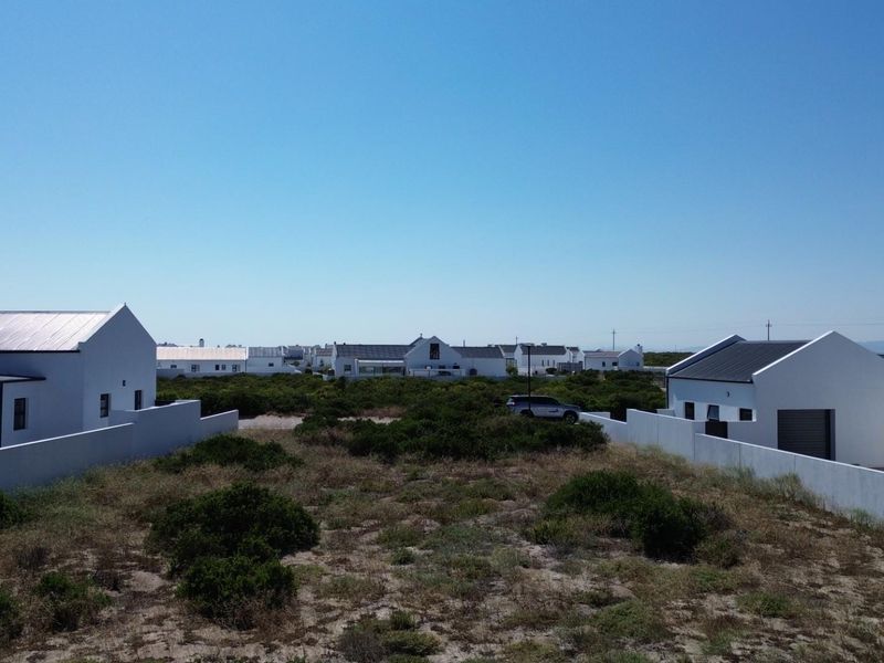 Aerial view of a residential plot featuring surrounding white-walled homes with metal roofs and natural coastal vegetation.