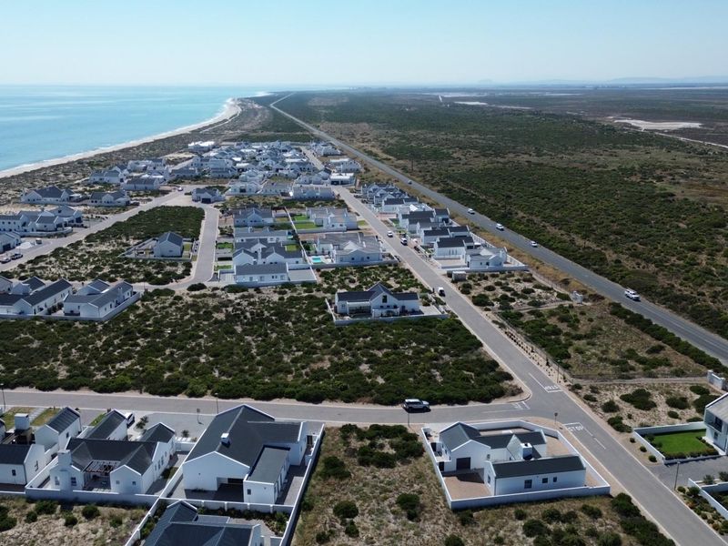 An aerial view of a coastal residential estate featuring modern white homes, paved streets, and proximity to the coastline.