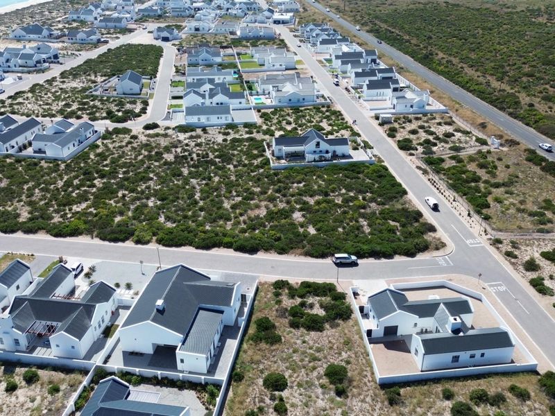 An aerial view of a coastal residential estate featuring modern homes, paved streets, and surrounding natural vegetation near the coastline.