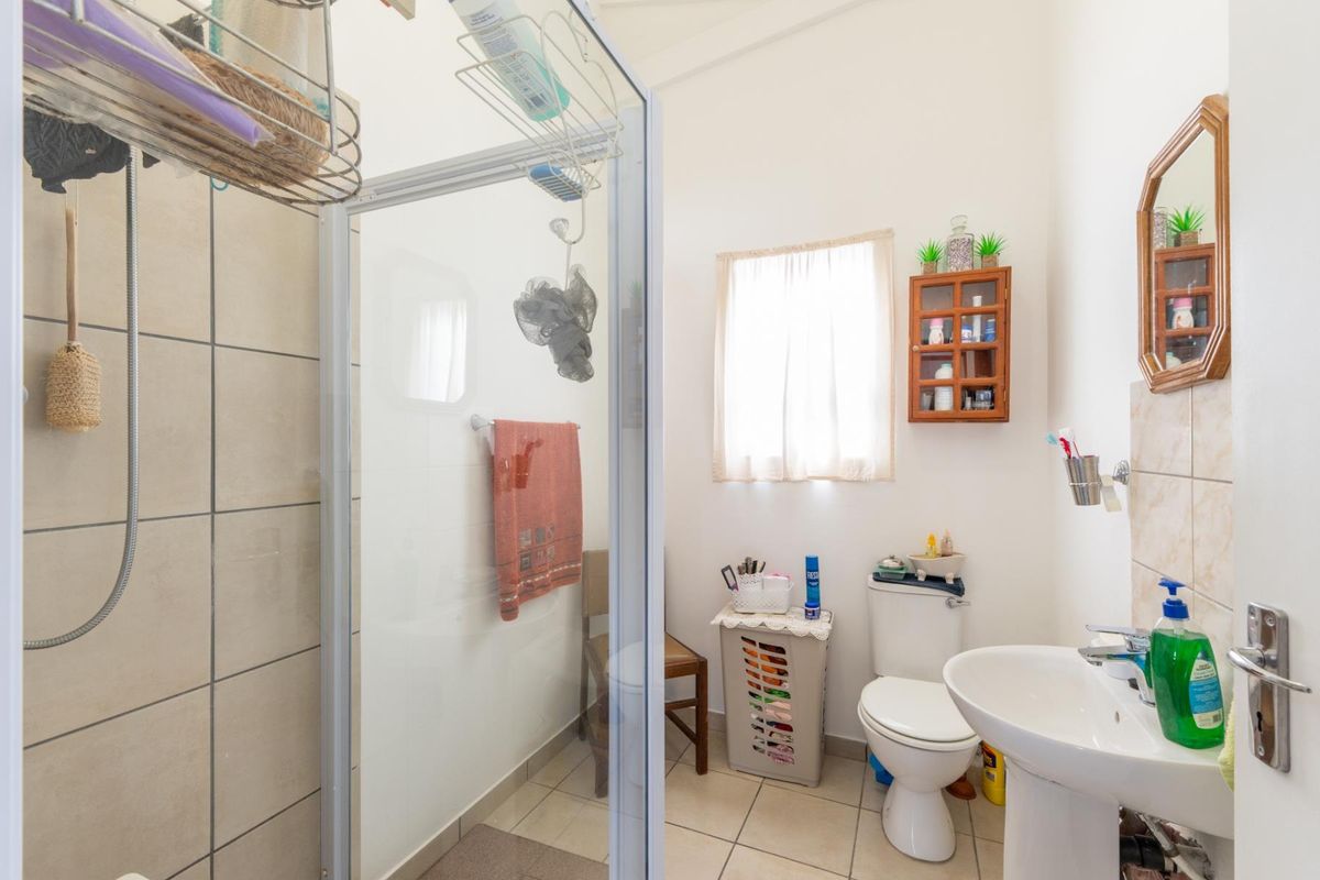 A functional bathroom featuring a shower enclosure, pedestal basin, and toilet with neutral tiled flooring and wall finishes.