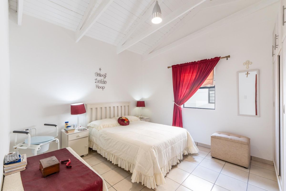 A bright bedroom featuring a vaulted ceiling, tiled flooring, and built-in cupboards, offering a clean and functional living space.