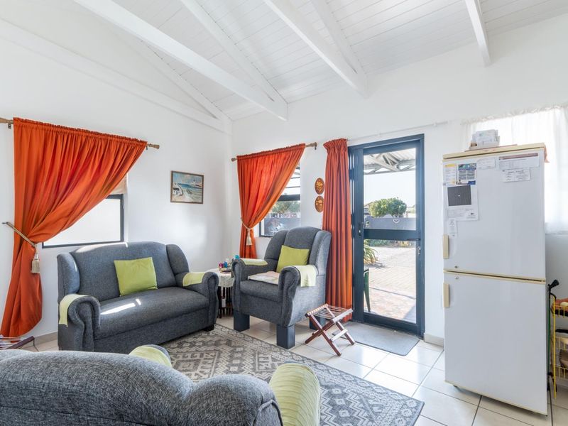 A bright living room featuring a vaulted ceiling with exposed beams, tiled flooring, and direct access to the outdoor patio area.