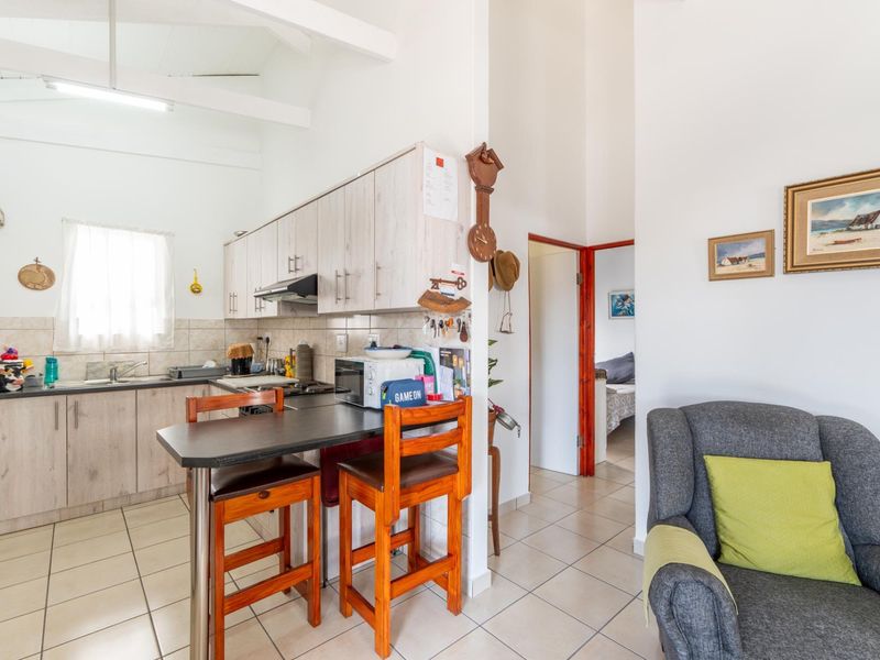 Open plan kitchen area featuring light wood-look cabinetry, tiled backsplash, and a breakfast bar, seamlessly flowing into the adjacent living space.