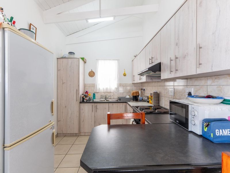 Functional kitchen featuring light wood-look cabinetry, dark laminate countertops, tiled backsplash, and exposed white rafters, providing a bright and practical cooking space.