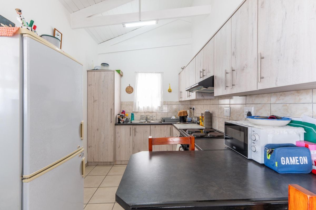 Functional kitchen featuring light wood-look cabinetry, dark laminate countertops, tiled backsplash, and exposed white rafters, providing a bright and practical cooking space.