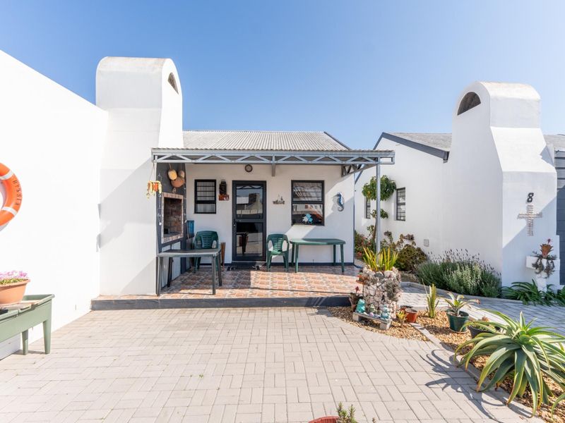 A covered patio area featuring a built-in braai, tiled flooring, and a metal roof awning, set within a paved courtyard.