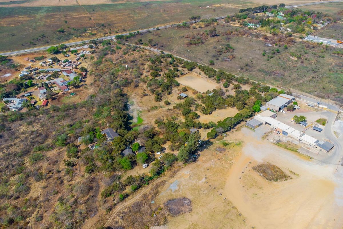 An aerial view of a large rural property featuring multiple outbuildings, expansive grounds, and gravel access roads set within a natural landscape.