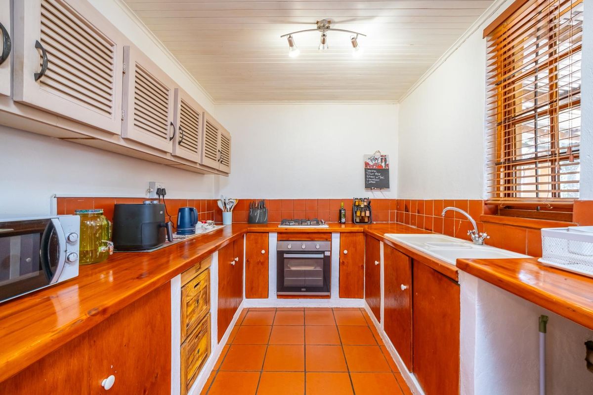 A functional kitchen featuring timber cabinetry, wooden countertops, a built-in oven with gas hob, and a double sink with tiled splashback.