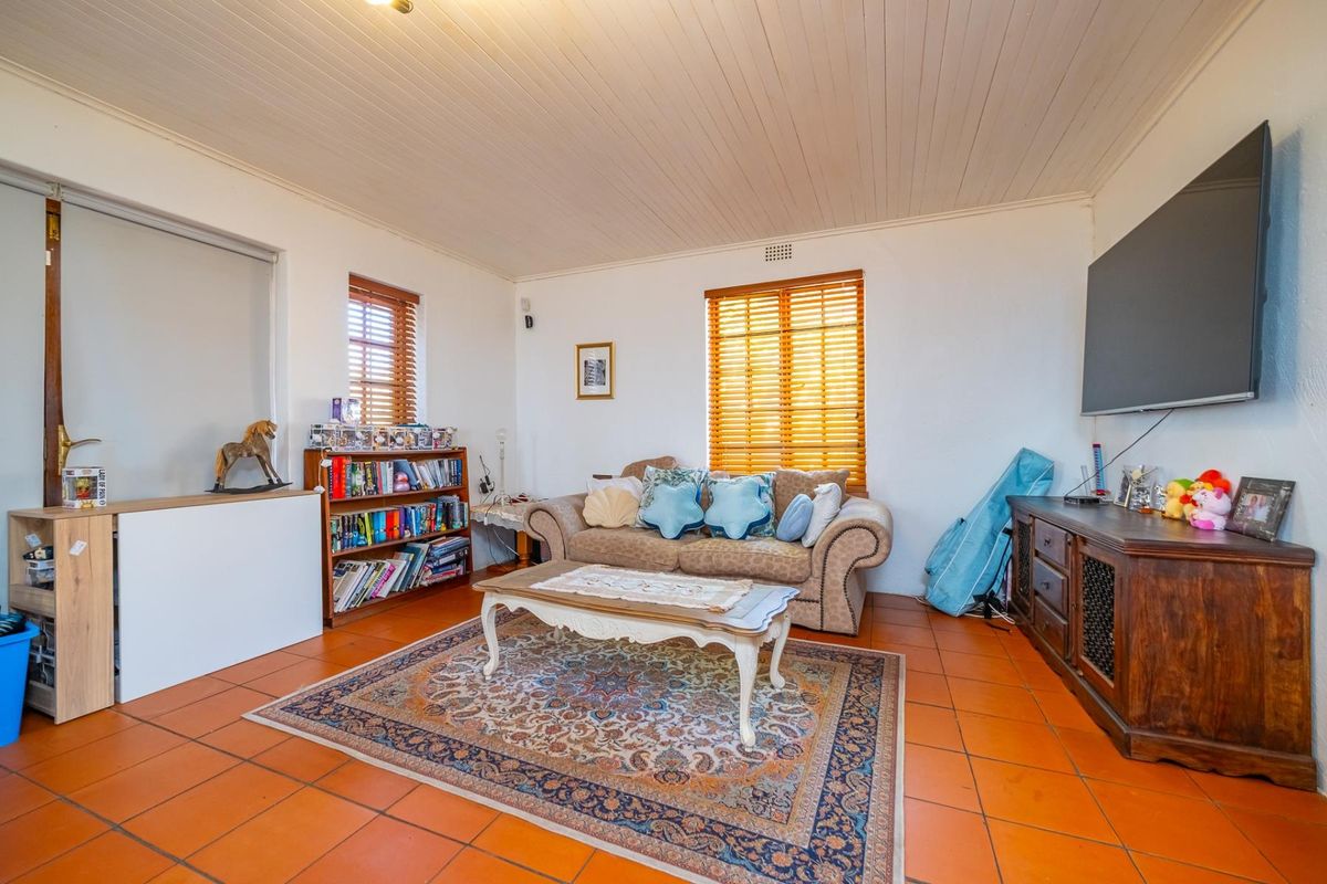 A comfortable living room featuring terracotta floor tiles, a timber-look ceiling, and natural light through venetian blinds.