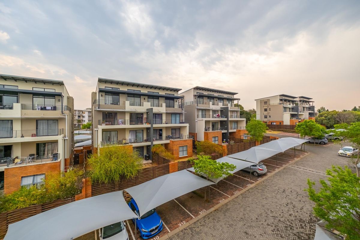 Aerial view of a modern apartment complex featuring multi-story residential buildings, private balconies, and designated covered parking bays within a landscaped estate.