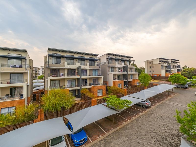Aerial view of a modern apartment complex featuring multi-story residential buildings, private balconies, and designated covered parking bays within a landscaped estate.