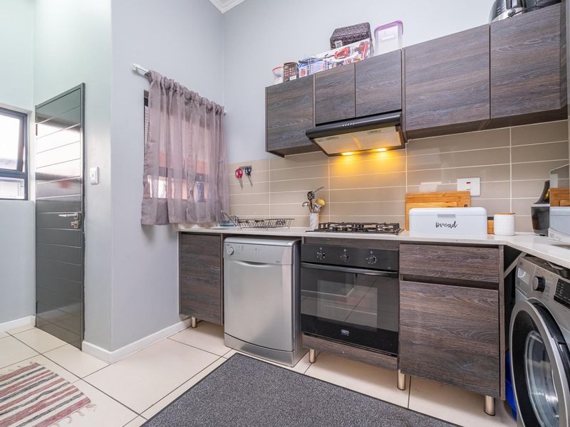 Compact kitchen featuring dark wood-look cabinetry, gas hob, electric oven, extractor fan, and tiled backsplash with neutral floor tiles.