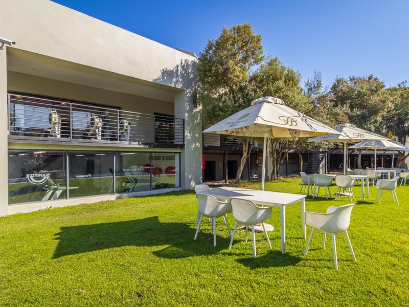 A well-maintained communal garden area featuring a manicured lawn, outdoor seating, and views of the building's fitness facility with large glass windows.