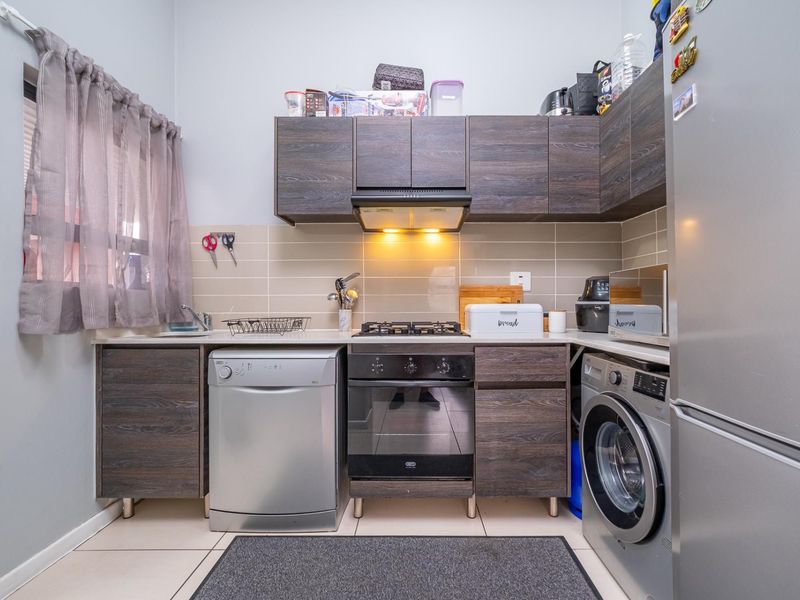 Compact kitchen featuring dark wood-look cabinetry, a gas hob with extractor fan, tiled backsplash, and integrated space for laundry and dishwashing appliances.