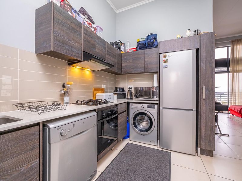 Compact modern kitchen featuring dark wood cabinetry, gas hob, extractor fan, under-counter oven, and tiled finishes, seamlessly integrated into the open-plan living area.