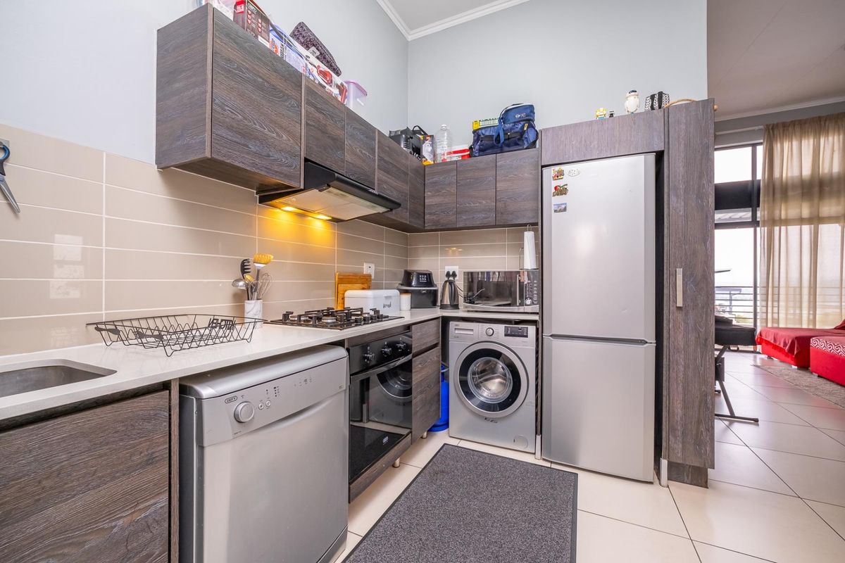 Compact modern kitchen featuring dark wood cabinetry, gas hob, extractor fan, under-counter oven, and tiled finishes, seamlessly integrated into the open-plan living area.