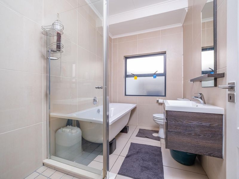 A well-maintained bathroom featuring a glass-enclosed shower, a bathtub, a modern vanity with basin, and neutral wall and floor tiling.